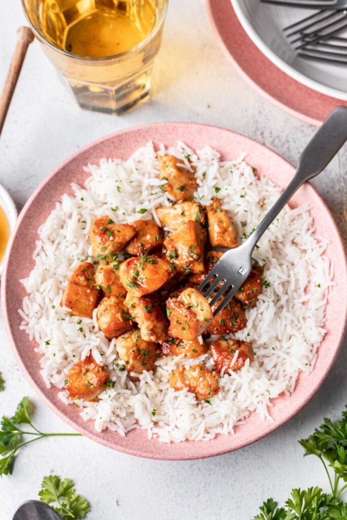 honey butter chicken on a bed of rice served on a pink plate with a fork