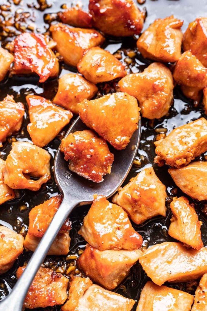 up close photo of chicken in a pan covered with sauce with 2 pieces on a spoon