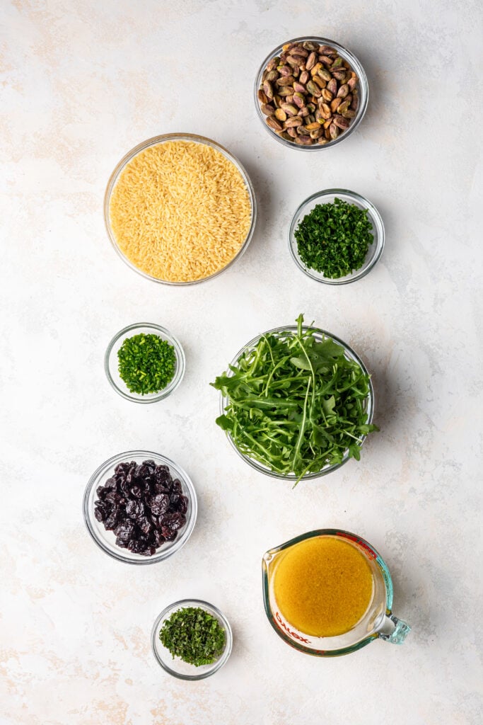 ingredients in bowls such as orzo, fresh herbs, dried cherries, nuts and dressing