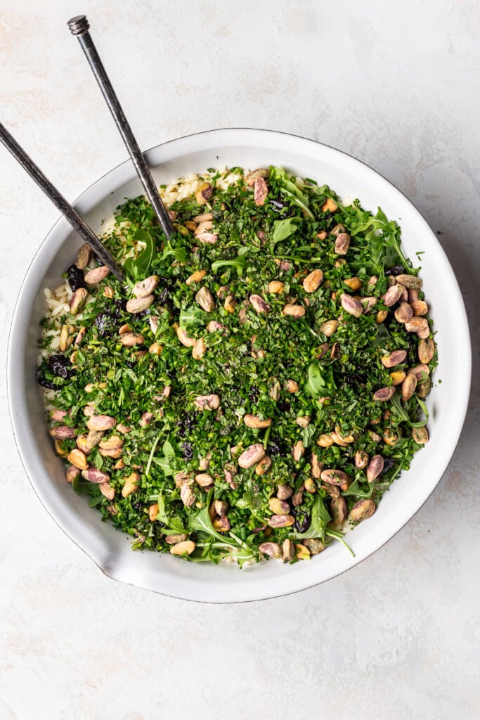 orzo in a large white bowl with lots of fresh herbs and nuts on top