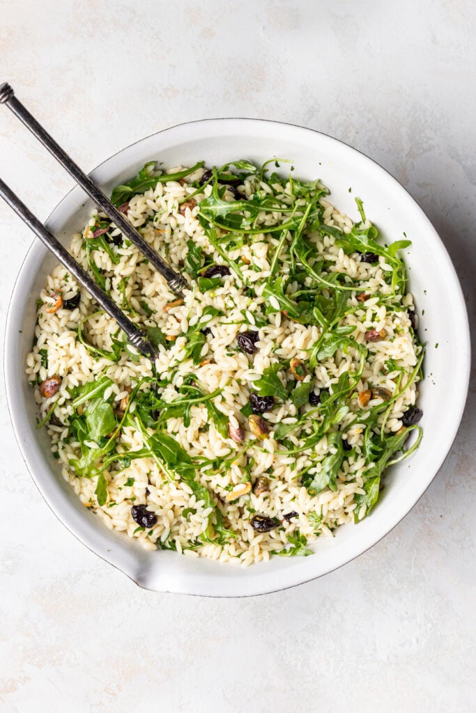 orzo salad with fresh herbs, arugula and dried cherries with serving spoons
