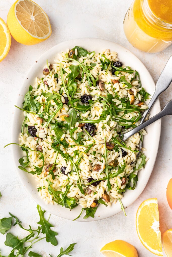 orzo salad on a white platter with serving spoons