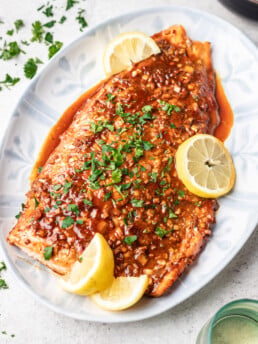 cooked salmon on a white platter with sauce and sliced lemons