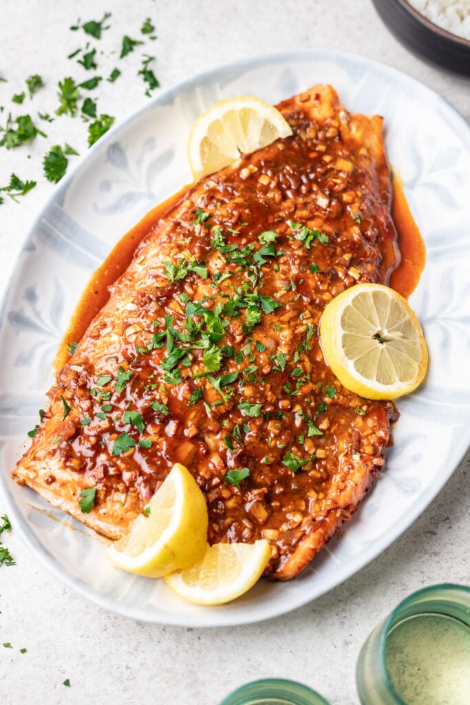 cooked salmon on a white platter with sauce and sliced lemons