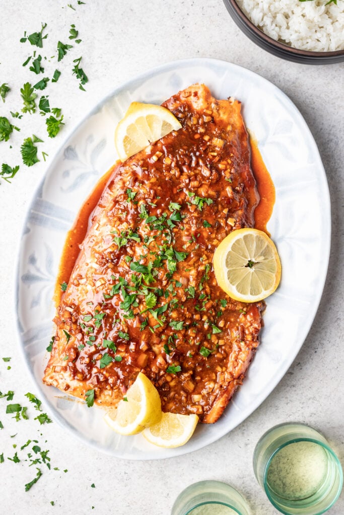 whole cooked salmon on a white platter with sauce and sliced lemons
