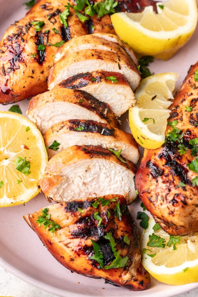 sliced grilled chicken on a pink plate with lemons