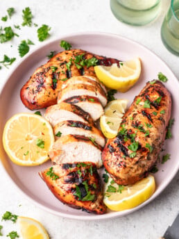 sliced grilled chicken on a pink plate with lemons