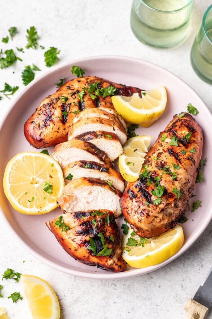 sliced grilled chicken on a pink plate with lemons