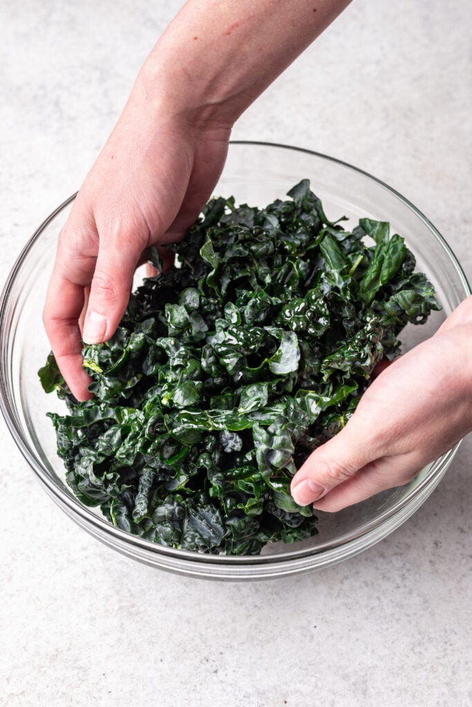 two hands tossing dressing into kale