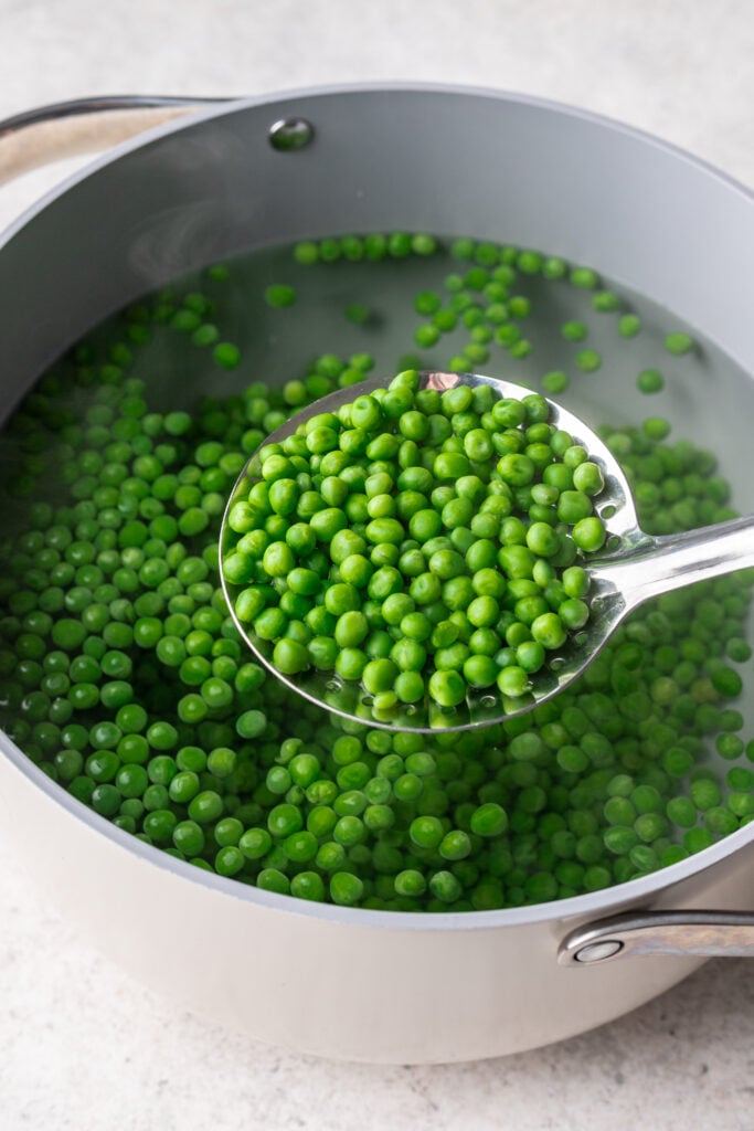a strainer holding peas over a pot of boiling water with peas