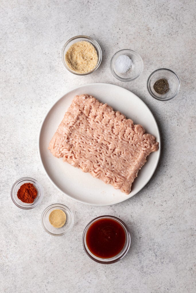 raw ground chicken on a plate with ingredients in small bowls all around