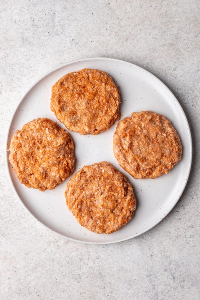 4 raw chicken burger patties on a plate