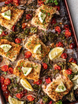 pieces of salmon on a sheet pan with cooked broccolini and tomatoes