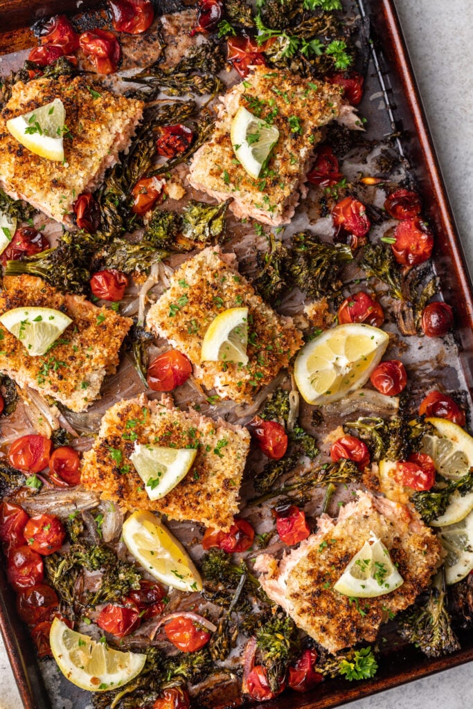pieces of salmon on a sheet pan with cooked broccolini and tomatoes