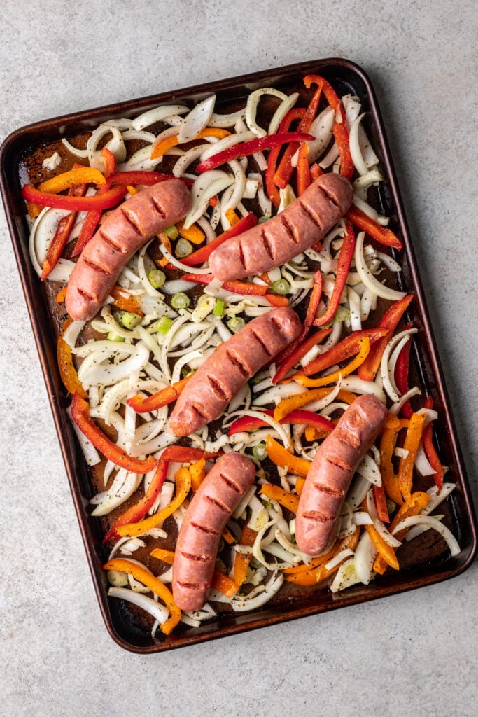 sheet pan with sliced raw veggies and sausages