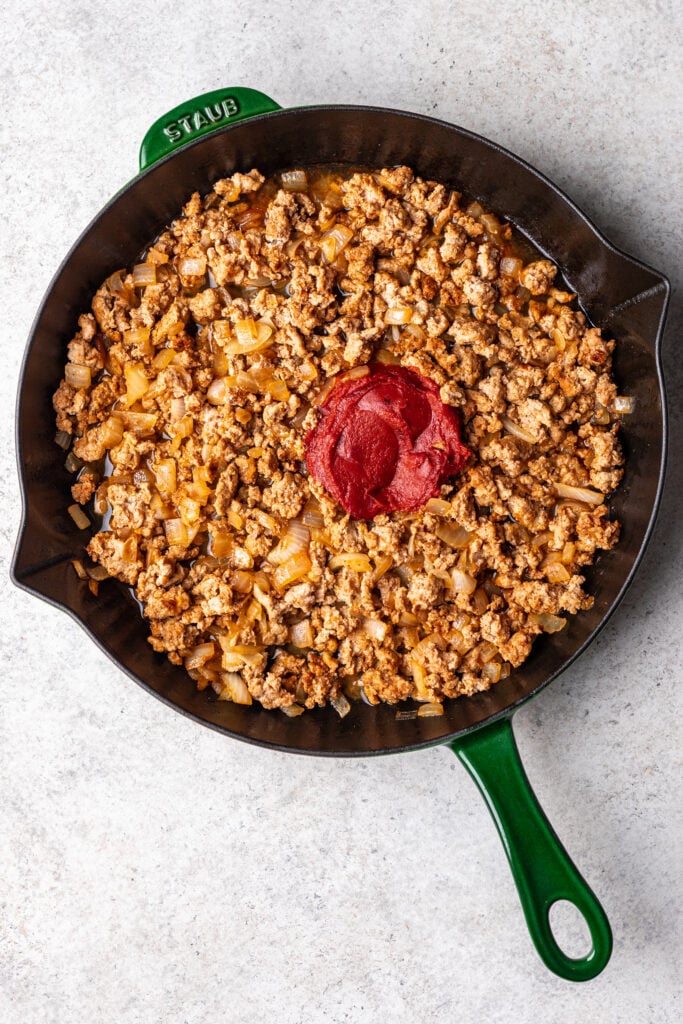 sauteed ground turkey in a pan with a scoop of tomato paste