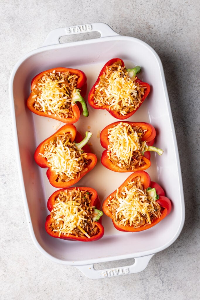 red bell peppers cut in half in a white dish with ground turkey filling and cheese on top