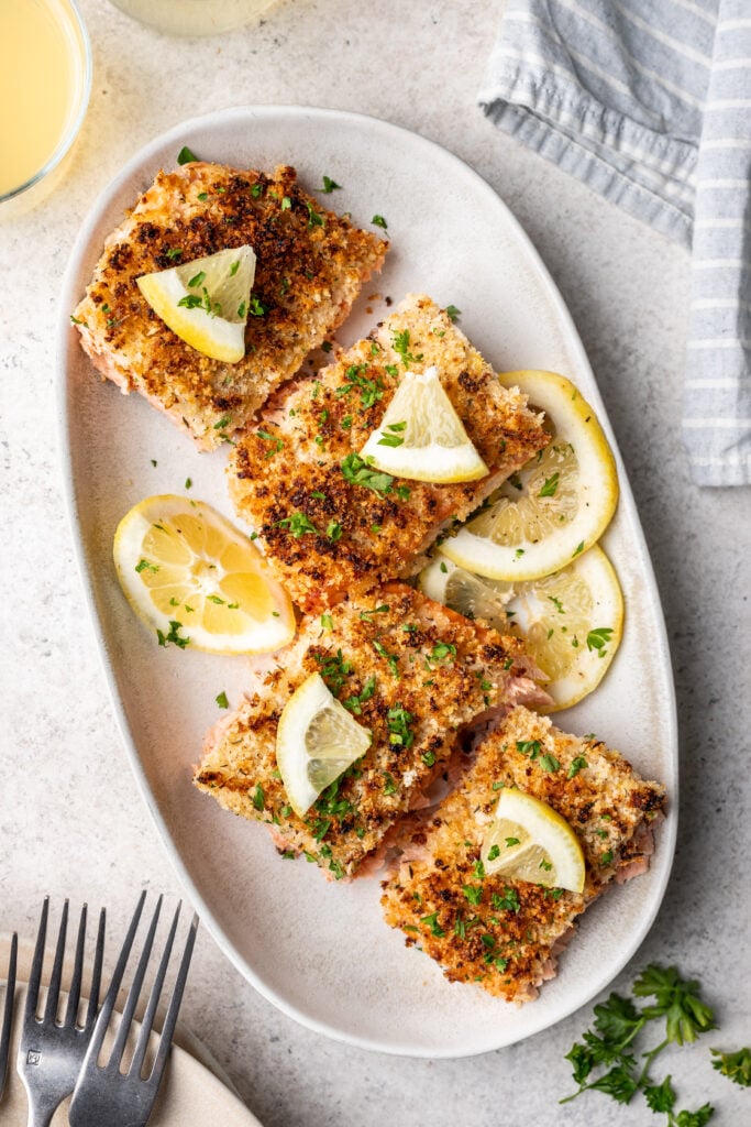 sliced panko crusted salmon on a white oval platter with lemon slices