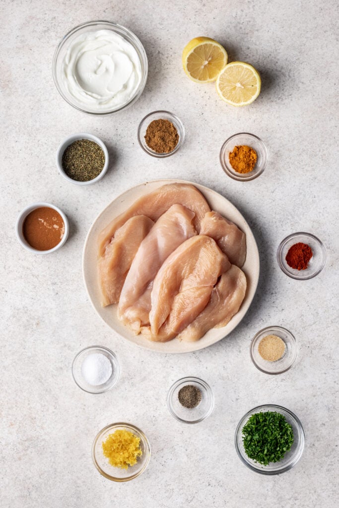 Ingredients in bowls like chicken breasts, spices and yogurt