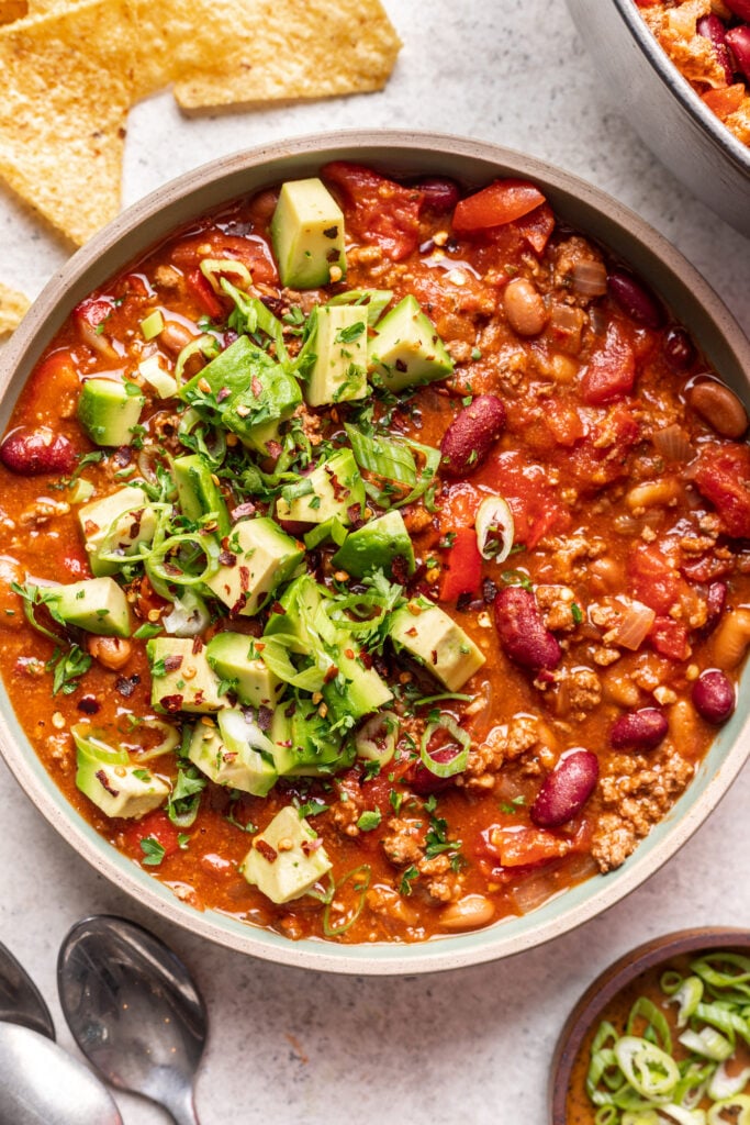 a bowl of ground beef chili with avocado and green onions