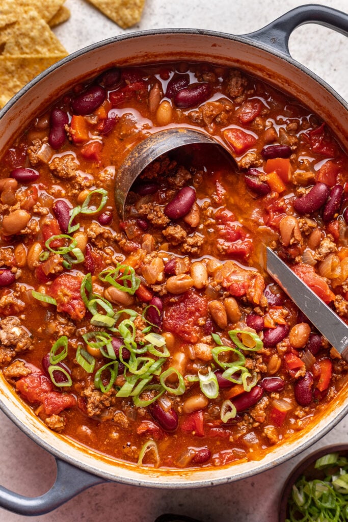 chili with a ladle and sliced green onions in a pot