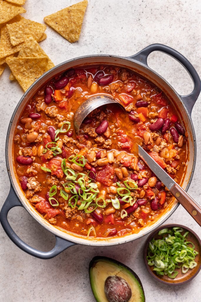 chili with a ladle and sliced green onions in a pot