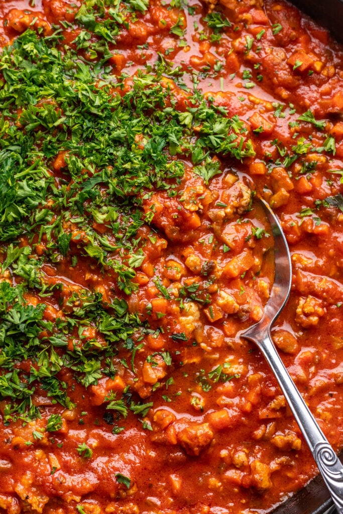 ground chicken bolognese sauce in a skillet with chopped parsley and a spoon