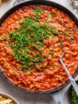 ground chicken bolognese sauce in a skillet with chopped parsley and a spoon