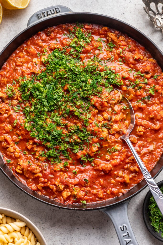ground chicken bolognese sauce in a skillet with chopped parsley and a spoon