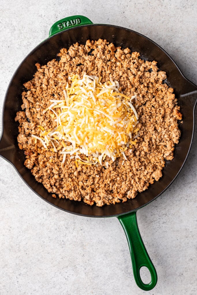 ground turkey cooked with spices in a cast iron skillet with shredded cheese on top
