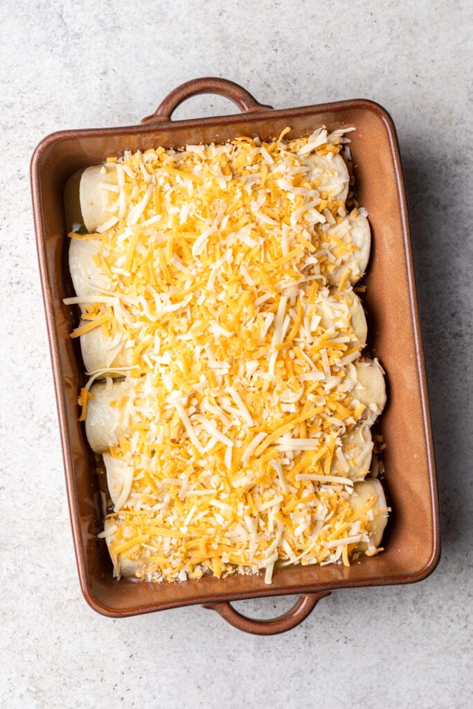 6 tortillas rolled up next to each other in a baking dish topped with cheese