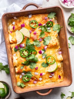 green enchiladas in a baking dish with melted cheese, cilantro, onion and jalepeno