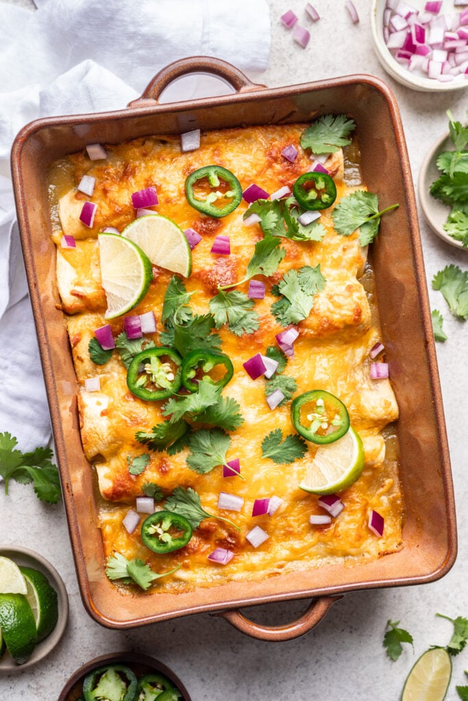 green enchiladas in a baking dish with melted cheese, cilantro, onion and jalepeno