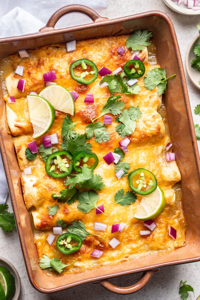 green enchiladas in a baking dish with melted cheese, cilantro, onion and jalepeno