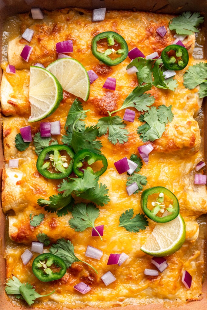 green enchiladas in a baking dish with melted cheese, cilantro, onion and jalepeno