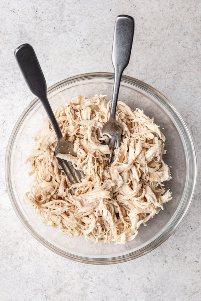 shredded chicken in a glass bowl with 2 forks