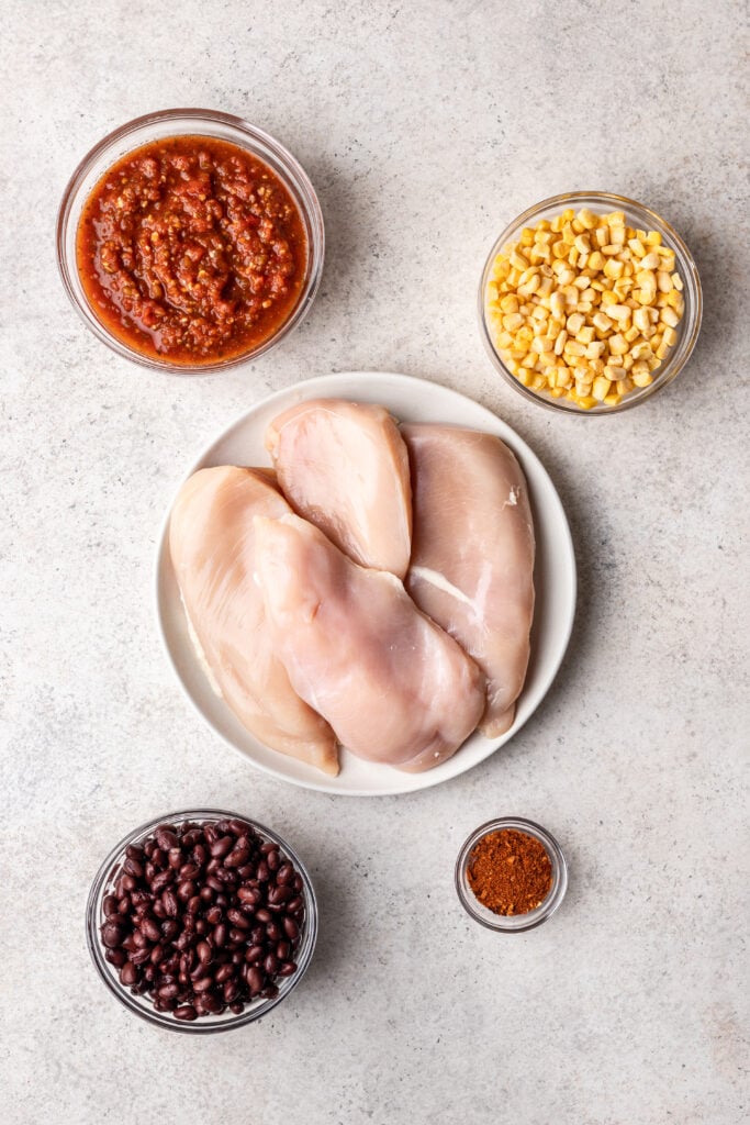 raw chicken breasts on a plate with bowls on ingredients around