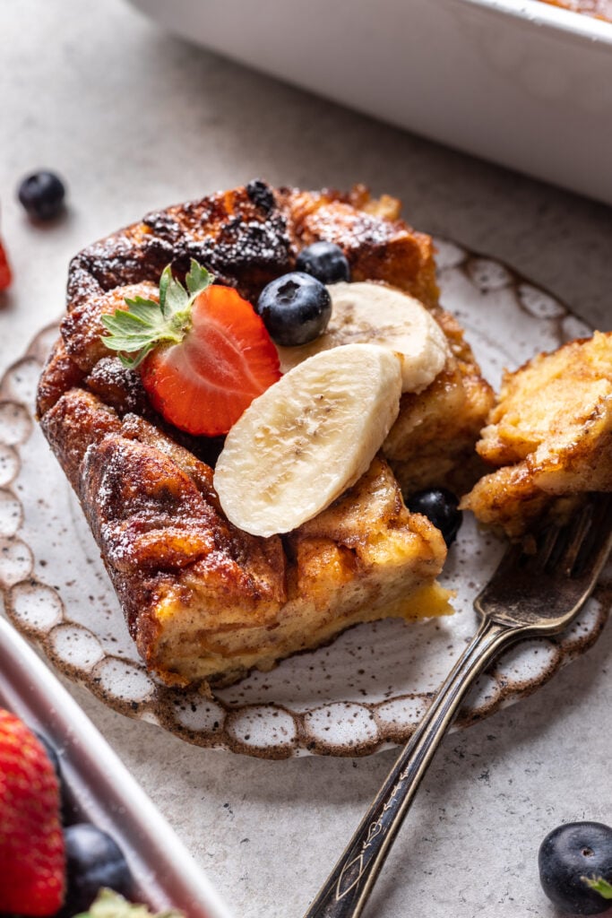 a slice of banana cinnamon french toast with banana and strawberries on top with a fork