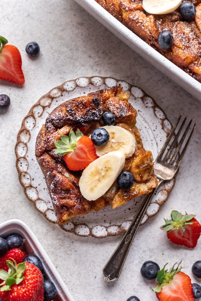 a slice of banana cinnamon french toast with banana and strawberries on top with a fork