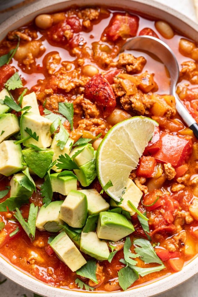 bowl of chicken chili with a spoon and topped with avocado and a lime