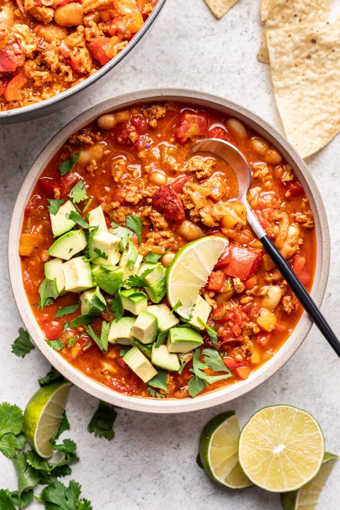 bowl of chicken chili with a spoon and topped with avocado and a lime
