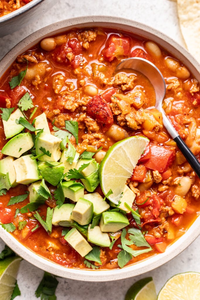 bowl of chicken chili with a spoon and topped with avocado and a lime