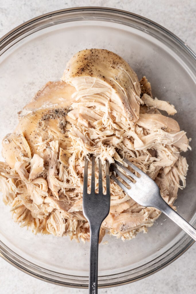 shredded chicken in a glass bowl with two forks