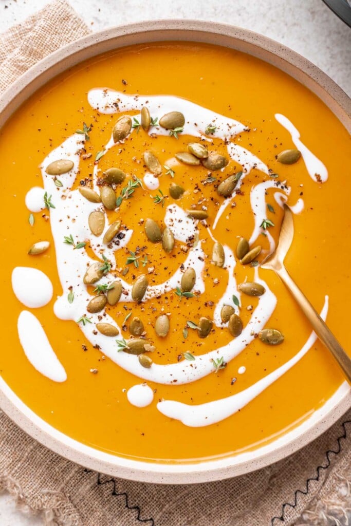 butternut squash soup in a bowl with creme fresh drizzle and pumpkin seeds and a spoon