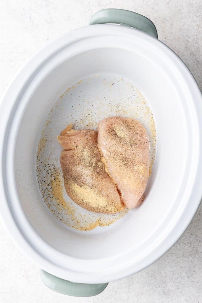 2 raw chicken breasts in a slow cooker with spices