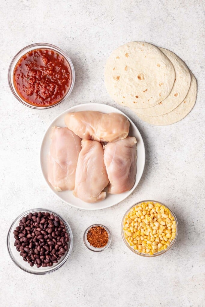 ingredients in bowls like raw chicken, black beans, salsa, tortillas and corn
