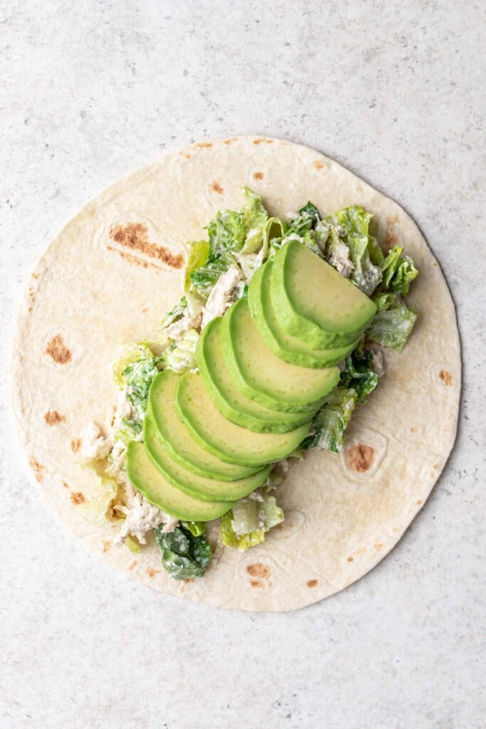 chicken caesar salad on top of a tortilla with sliced avocado