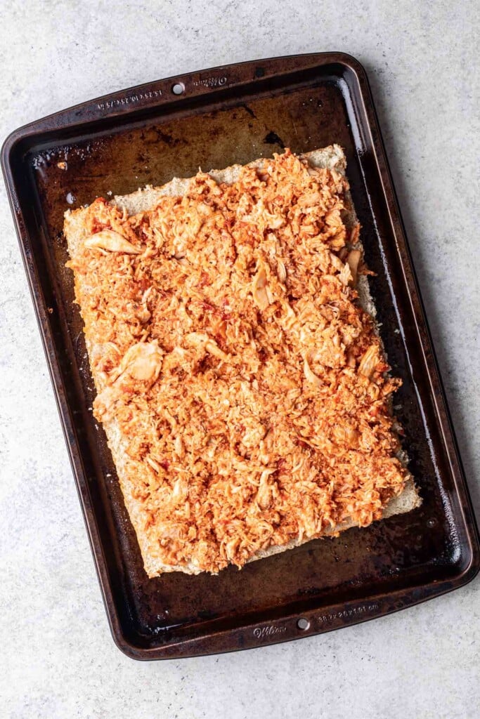 shredded chicken mixed with sauce on bread on a sheet pan