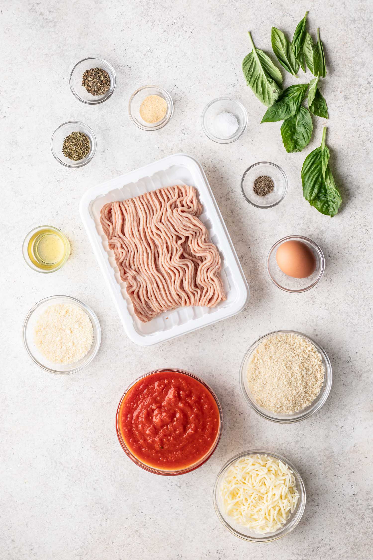 ground chicken, marinara sauce, egg and other ingredients on a grey background