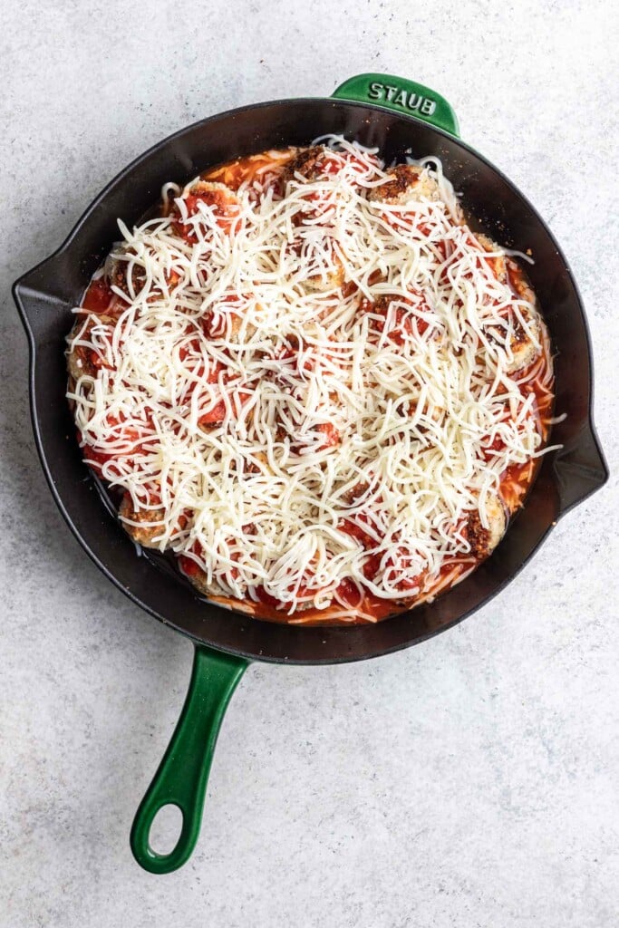 meatballs in a skillet with sauce and shredded cheese